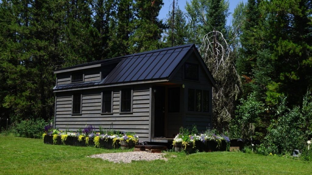Black wooden house with a flower garden, perfect for freelancers looking for peace and quiet.